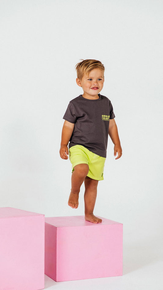 Animal Crackers Skate Club Tee. In charcoal with lime print this tee will be a wardrobe staple. A crew neck with domes across the left shoulder makes for easy dressing. A logo on the chest and back print of Animal Crackers Raccoon skateboarding in the sun makes this tee so cool for any little one. Sizes 0-5.